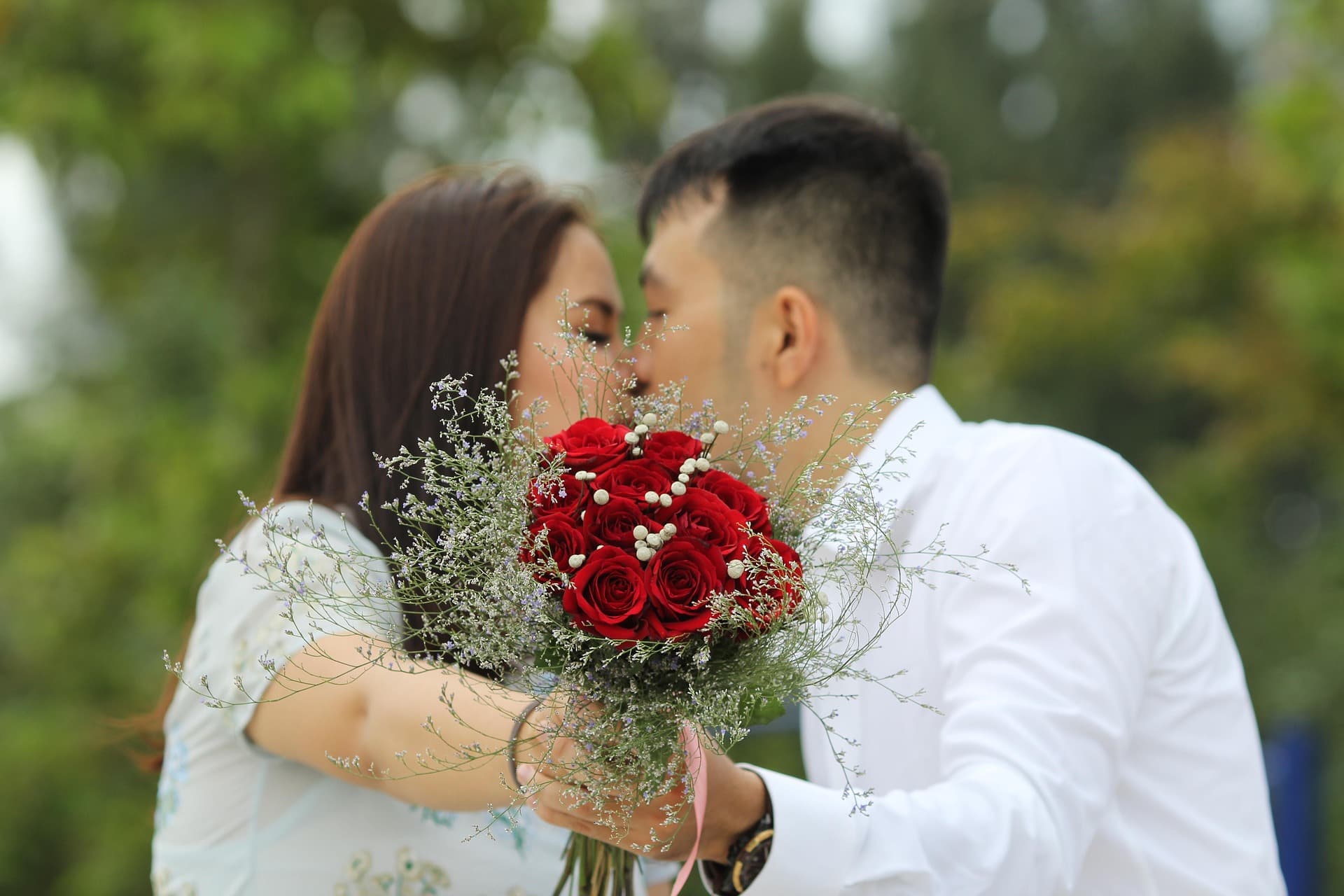 Una pareja besándose detrás de un ramo de rosas rojas