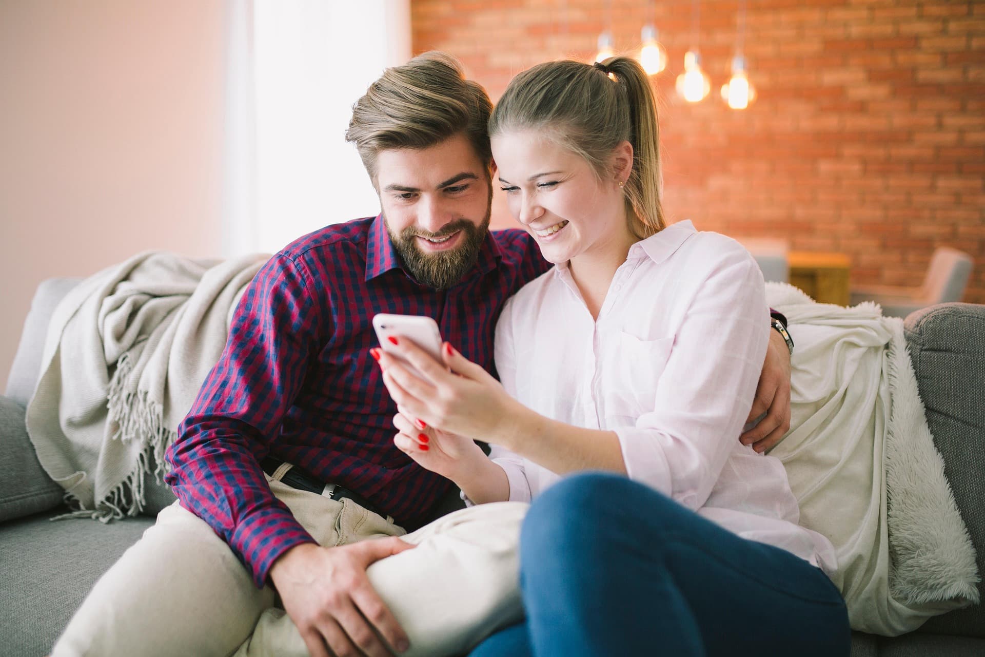 Una pareja sonriendo juntos ante un teléfono en el sofá